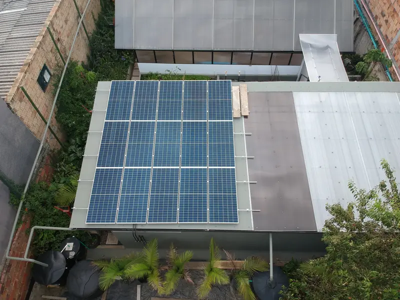 Vista cenital de la cubierta de un negocio en Bogotá con un arreglo de paneles solares, junto a un patio con palmas