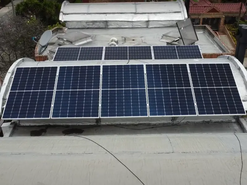 Dos filas de paneles solares sobre la cubierta curva de una casa en Bogotá, entre edificios de ladrillo