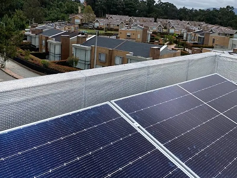 Paneles solares sobre la terraza de una casa en Bogotá, con un conjunto de casas de ladrillo y árboles al fondo