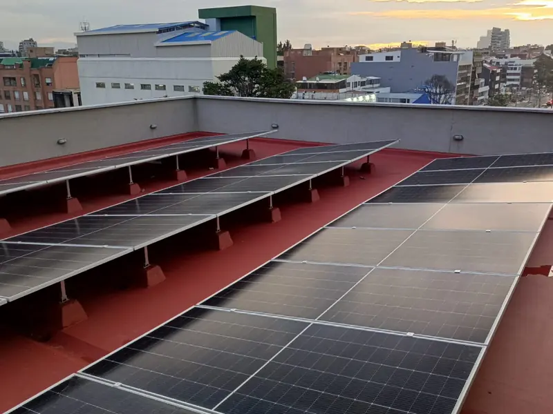 Filas de paneles solares sobre la terraza roja del edificio Box Office, en Bogotá, con la ciudad al atardecer