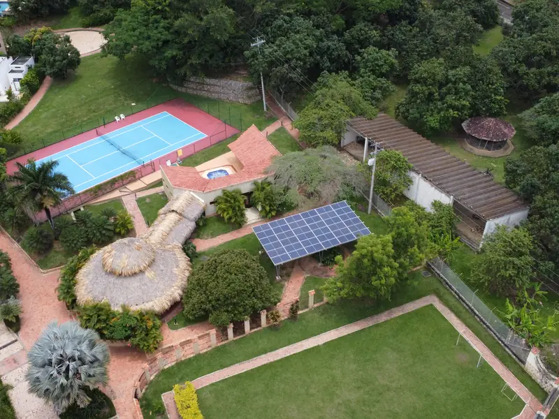 Vista aérea de las zonas comunes de Madremonte, en Anapoima, con una pérgola de paneles solares entre la cancha de tenis, los kioscos y la cancha de fútbol