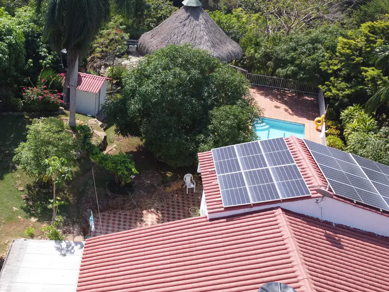 Vista aérea de una casa con techo de teja en Turbaco, Bolívar, con paneles solares en dos caras de la cubierta y una piscina entre los árboles