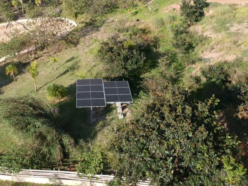 Paneles solares montados en el suelo, entre árboles y pasto, en un terreno de Villa de Leyva, Boyacá